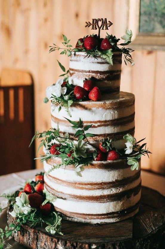 a naked wedding cake with fresh strawberries, greenery and white blooms plus a topper for a summer rustic wedding