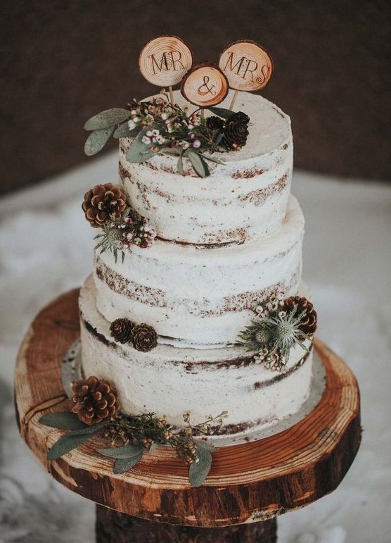 a naked wedding cake with thistles, pinecones, berries, wood slice toppers for a cozy winter wedding