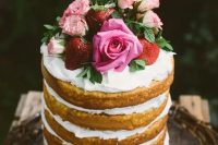 a naked wedding cake with whipped cream, fresh strawberries and pink roses for a garden summer wedding
