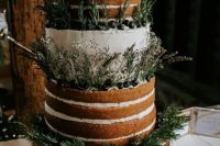 a partly naked wedding cake with lots of greenery, wildflowers and fresh berries for a rustic wedding
