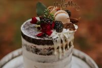 a pretty fall chocolate naked wedding cake with creamy drip, blackberries, macarons, figs, red blooms and a gold calligraphy topper