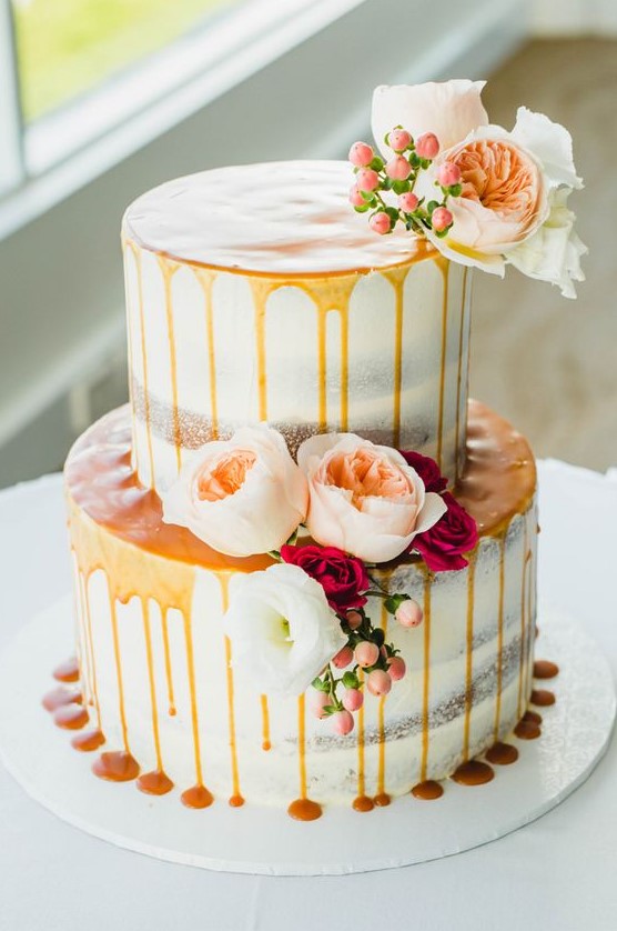 a pretty fall two-tier wedding cake with caramel drip, pastel blooms and berries is a lovely and delicious idea