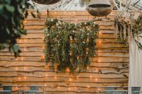 a reclaimed wood wall, greenery and blooms and lights hanging down to create a cozy and intimate wedding ceremony space