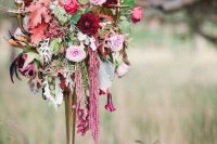 a refined and moody Halloween wedding centerpiece of a tall candlelabra with black candles, pink and burgundy blooms and greenery