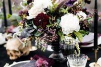 a refined and moody Halloween wedding centerpiece of white, burgundy and deep purple blooms, greenery and leaves plus a table number