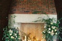 a refined fireplace with candles all around and lush greenery and white blooms incorporated