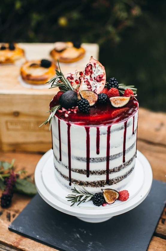 a semi naked wedding cake with pomegranate drip topped with fruits and greenery for a decadent fall wedding