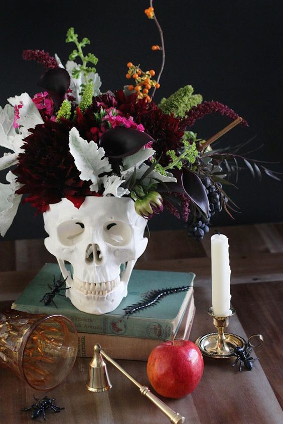 a stack of books, a skull with a dark floral arrangement with dark burgundy florals, pale and saturated greenery and berries