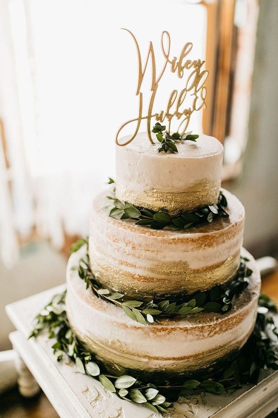 a stylish naked wedding cake with gold leaf, greenery and an elegant topper for a modern wedding