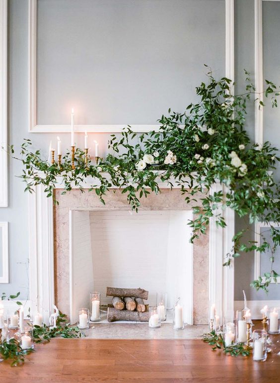 a subtle fireplace backdrop with candles around and on the mantel, with lush greenery and white blooms