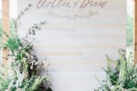 a whitewashed wooden wall with letters and monograms and greenery and bloom arrangements around