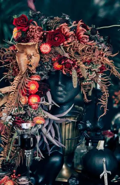 a wicked wedding centerpiece of a human bust topped with lush blooms in deep red, burgundy flowers and cascading dried greenery