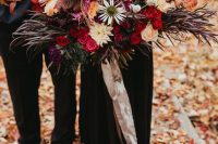 an oversized colorful wedding bouquet with red, pink, purple, peachy, orange blooms, dark foliage and greenery to stand out with a black wedding dress