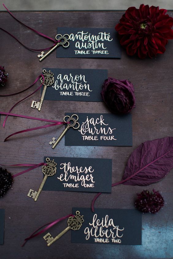 elegant matte black escort cards with gold calligraphy, vintage brass keys and moody blooms
