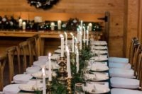 a Christmas tablescape with an evergreen runner, candles in gold candleholders, gold cutlery and emerald napkins