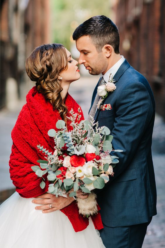 a Christmas wedding bouquet of red, blush and white blooms, greenery and with a catchy shape
