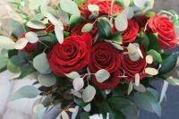 a Christmas wedding bouquet of red roses, greenery and a white wrap is very contrasting