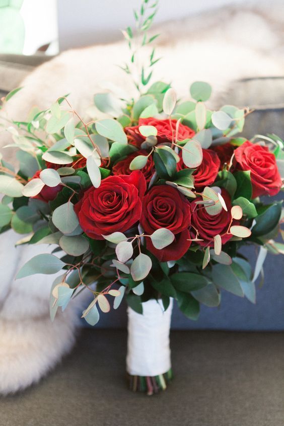 a Christmas wedding bouquet of red roses, greenery and a white wrap is very contrasting