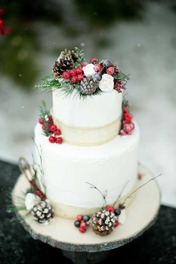 a Christmas wedding cake topped with fake greenery, berries, pinecones and burlap ribbons for a snowy feel