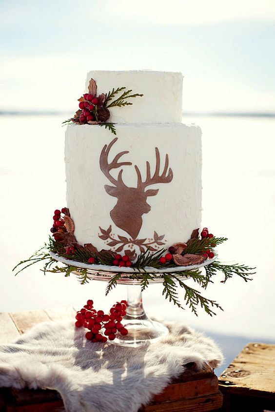 a Christmassy wedding cake with a deer silhouette, greenery, berries and nuts for a woodland wedding