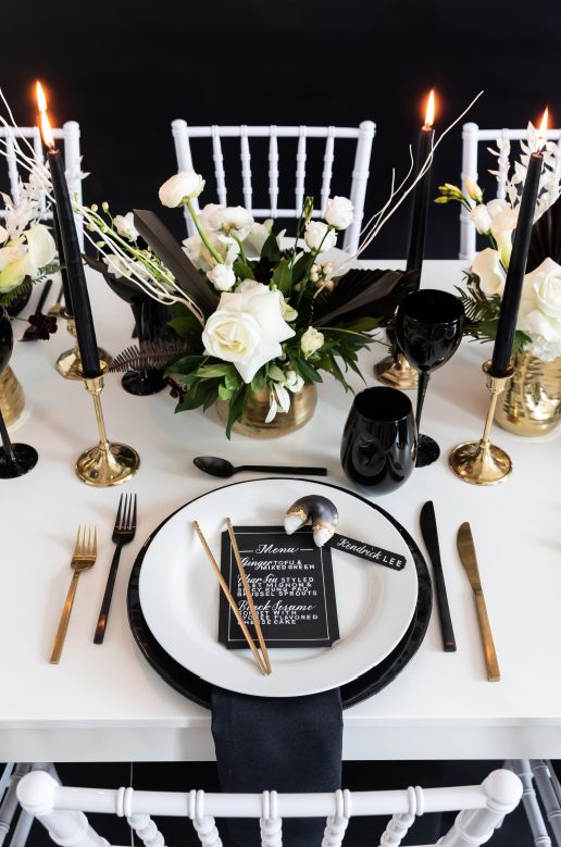 a beautiful black and white modern wedding centerpiece with white blooms and black dyed leaves and branches, tall and thin black candles