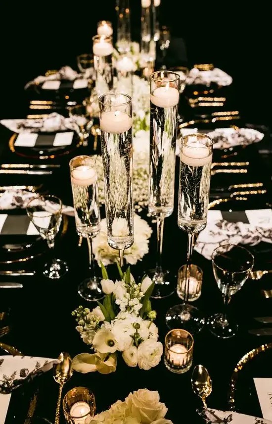 a black and white NYE wedding tablescape with black and white menus, white blooms, floating candles and gold cutlery