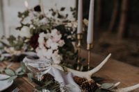 a boho woodland wedding centerpiece of greenery, neutral blooms, pinecones, tall and thin candles is a lovely idea