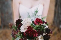 a bold Christmas wedding bouquet of blush, burgundy and deep purple blooms, berries and greenery