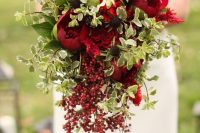 a bold Christmas wedding bouquet of red and burgundy blooms and greenery plus cascading berries for a catchy touch