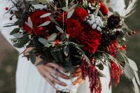 a bold Christmas wedding bouquet of red and deep purple blooms, greenery and berries is very chic