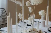 a bold and edgy minimalist wedding tablescape with neutral linens, black chargers and cutlery, neutral candles of various sizes and white blooms