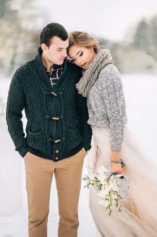 a bride wearing a blush wedding dress and a grey cable knit sweater plus a scarf over it for a cozy feel and look