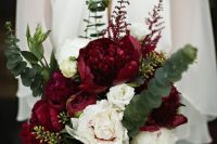 a bright Christmas wedding bouquet of burgundy and blush peonies and greenery that creates a bold shape