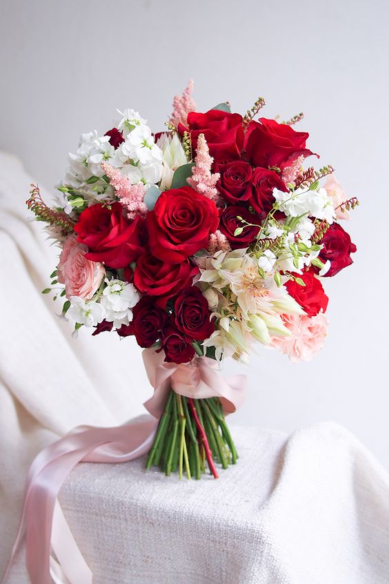 a bright Christmas wedding bouquet of red, burgundy and white and blush blooms plus some greenery