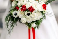 a bright traditional Christmas wedding bouquet of white and red blooms, greenery and red ribbons is a bold accessory