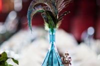 a bright wedding centerpiece of a blue bottle, feathers and peacock feathers for a Moroccan or boho wedding