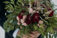 a chic Christmas wedding bouquet of greenery, eucalyptus, blush and burgundy blooms shows off much texture