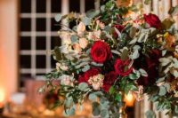 a chic Christmas wedding centerpiece of a gold stand with greenery, red and blush blooms and candles is wow