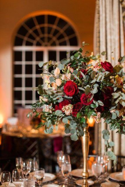 a chic Christmas wedding centerpiece of a gold stand with greenery, red and blush blooms and candles is wow