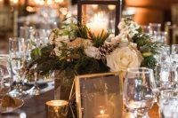 a chic Christmas wedding centerpiece of white blooms, fir branches, pinecones and a glass candle lantern is adorable