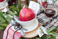 a chic rustic Christmas tablescape with a plaid runner and a striped napkin, greenery, pomegranates, tree stump candleholders and burgundy blooms