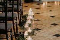 a chic wedding ceremony space with floating candles and greenery lining up the aisle and some florals at the altar
