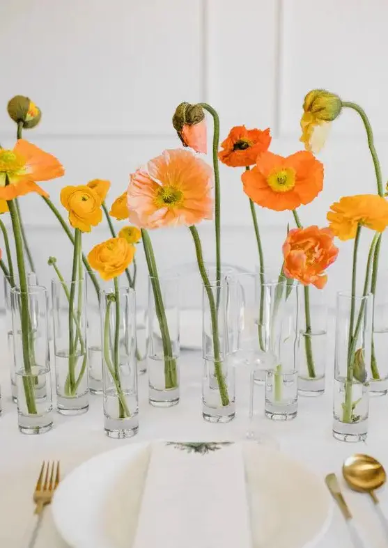 a cluster wedding centerpiece of glass vases and yellow ranunculus and orange and yellow poppies, one bloom in each vase