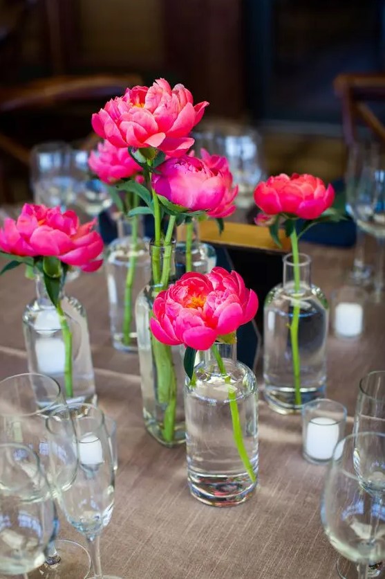 a cluster wedding centerpiece of magenta peonies and clear vases and candles is a lovely touch of color to your wedding reception