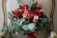 a colorful Christmas wedding bouquet of red and pink blooms, dark foliage and greenery plus berries