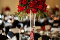 a colorful Christmas wedding centerpiece of a tall glass vase with petals and a candle and a bold floral and greenery arrangement