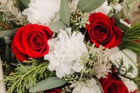 a contrasting Christmas wedding bouquet of red and white blooms, greenery and fir branches