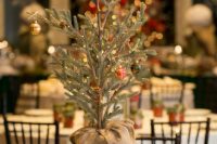a cool Christmas wedding centerpiece of a mini tree with pinecones and lights, a berry wreath and a framed table number