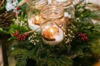 a cozy Christmas wedding centerpiece of fir branches, berries, blooms and candles in jars is warming up and cool