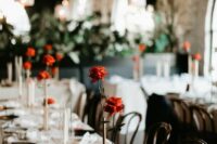 a creative modern wedding centerpiece of a brass metal vase with several tubes and red roses is accenting the table with color